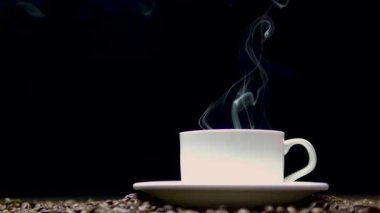 Siyah arka planda bir fincanda sade kahve, 4K 'de bir kahve fincanından duman. Fotokopi alanı olan kahve arka planı. Tahtadaki kahve çekirdekleri.