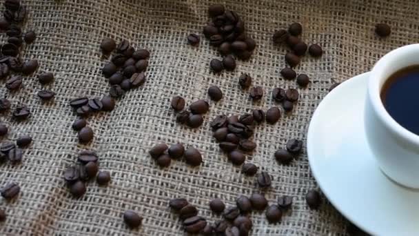 コーヒー豆と素朴な袋にコーヒーのカップ 木製のカフェで白いカップに黒コーヒーのトップビュー — ストック動画