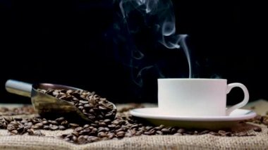 Ağır duman, kahve fincanı buharı 4K ağır çekimde. Siyah arka planda bir fincanda mis kokulu kahve. Eski bir tahta çuvalın üzerinde kahve taneleri. Kahve çekirdeği kızartıyorum.