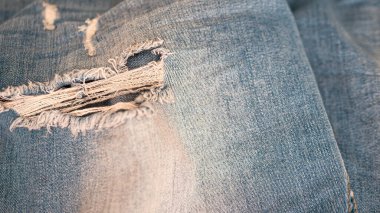 Jeans textiles. Denim background of blue fabric with frayed fabric. Blue ripped jeans close-up. Fabric background