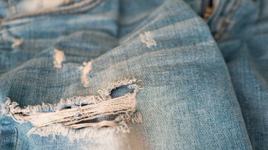 Jeans textiles. Clothing. Denim background of blue fabric with frayed fabric. Blue ripped jeans close-up. Fabric background