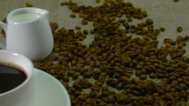 コーヒー豆で覆われたヴィンテージテーブルの上にカップの香りの黒いコーヒー — ストック動画