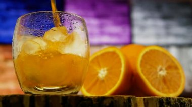 Barmen, buzlu bir bardağa sarı limonata, bar tezgahına bir kokteyl, renkli bir arka planda portakal suyu doldurur..