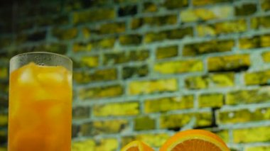 Şeffaf bardakta buzlu sarı limonata. Sarı tuğla bir duvarın arka planında portakal suyu.