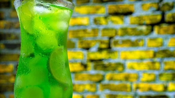 Buzlu, buzlu, soğuk limonata bardakta, duvarın arkasında. Kokteyl yeşil.