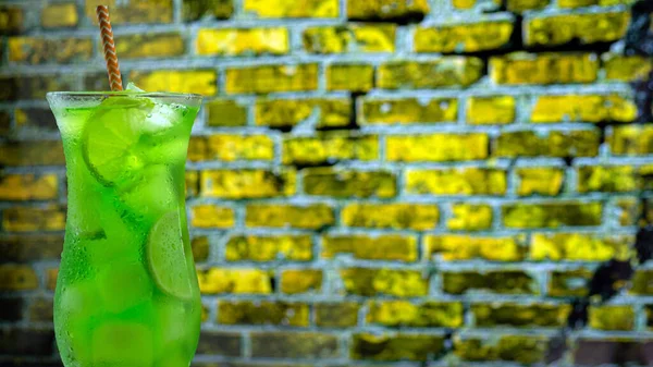 Cocktail in a glass on a brick wall background. Green lemonade with ice. Summer fresh drink in a tall glass