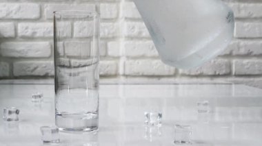 Şeffaf bir bardağa su dök, beyaz tuğladan bir arka plana soğuk maden suyu dök. Suda kabarcıklar.