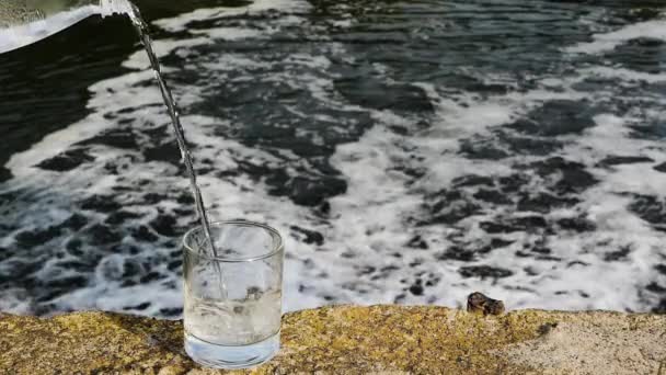 Gießen Sie Trinkwasser Ein Glas Vor Dem Hintergrund Eines Wasserfalls — Stockvideo