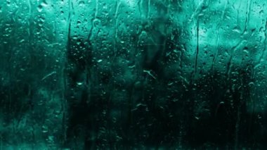 Mentolün turkuaz tonunda cam üzerindeki yağmur damlalarının yumuşak odak arkaplanı. Alan arkaplanını su damlalarıyla kopyala, pencerenin dışına güzel yağmur yağdır