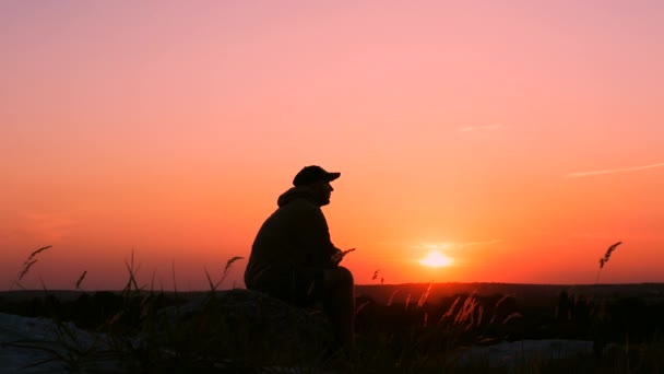 日没時には山の上の哀れな若者 座っている男は 日没を楽しんで落ち込んで男 山の上の男の悲しいシルエット — ストック動画