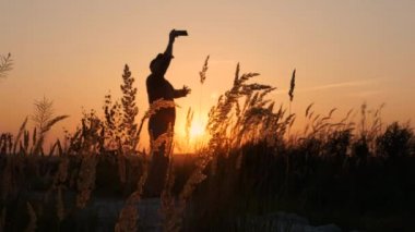 Dünyanın en mutlu insanı. Mutlu bir adamın silueti elinde akıllı bir telefonla selfie çekiyor, güzel bir günbatımının arka planına karşı duran bir adamın.