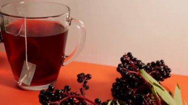 Şeffaf cam bardakta Elderberry kırmızı çayı, kırmızı bitki çayı, çay fincanıyla olgun mürver üzümü.