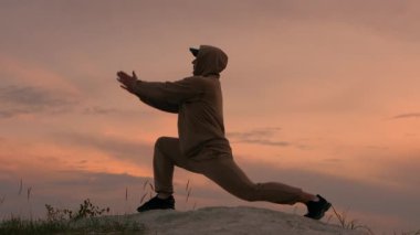 Bir adam gün batımında bir dağın tepesinde yoga yapıyor, bir adam doğada pilates yapıyor. Sporcu profesyonel egzersizler yapar.