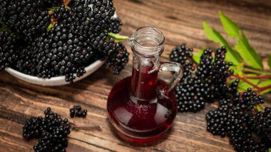 Ahşap bir arka planda olgun mürver, mürver böğürtlenlerinden çay ya da bitkisel tentür, böğürtlenlerden tıbbi ilaç