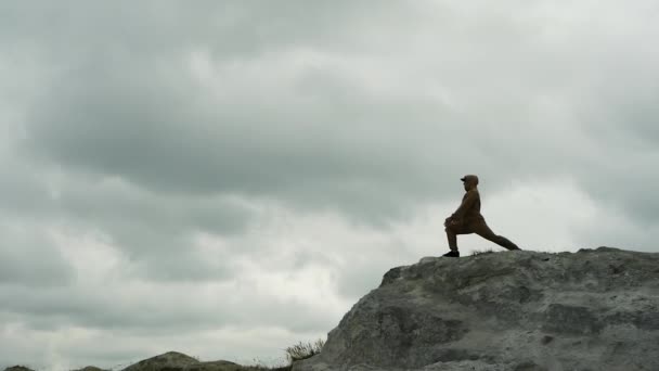 在灰色雨云的背景下 一个人在山顶上做瑜伽 一个人在大自然中做普拉提 运动员专业从事体操运动 — 图库视频影像