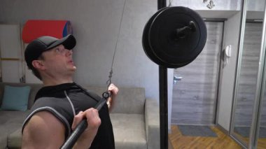 Genç ve yakışıklı sporcu sırt kaslarını ağır bir simülatörle şişiriyor. Modern apartmanlarda evde antrenman. Yavaş çekim