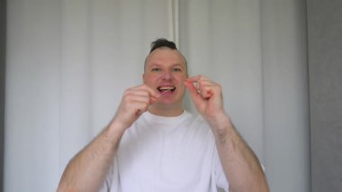 Genç bir adam dişlerini diş ipiyle fırçalar. Ağır çekim. Diş sağlığı konsepti.