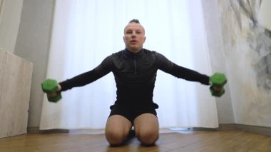 Erkek kolu ve omuz egzersizi. Evde egzersiz yaparken dambılları kaldırın. Kollarınızı dambıllarla sallayın. Yavaş çekim