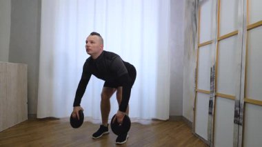 Genç adam ağır bir ağırlıkla kollarını ve omuzlarını pompalıyor. Ellerinde disklerle evde çalış. Yavaş çekim