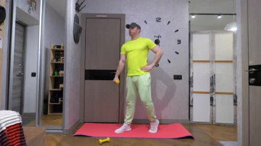 Aletlerin içinde erkek egzersizi. Fitness antrenmanı, elinde dambıllarla bir spor paspasının üzerinde. Yavaş çekim