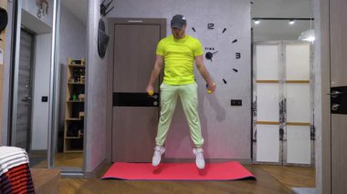 Zıplayan bir paspasın üzerinde spor yapmak. Ellerinde dambıllar olan bacaklar. Evde bacak egzersizi. Yavaş çekim