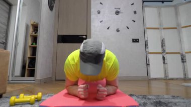 Spor salonunun paspası üzerinde antrenman. Genç adam pompalanıyor ve kalas egzersizi yapıyor. Yavaş çekim