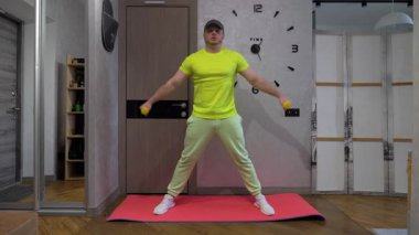 Ellerinde dambıllarla erkek antrenmanı, evde spor paspası, omuzlarını dambıllarla şişirmek, kollarını açmak..