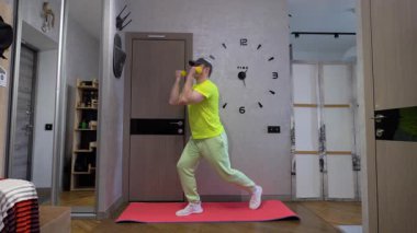 Ellerinde dambıllarla erkek antrenmanı, evde spor paspası, omuzlarını dambıllarla şişirmek, kollarını açmak.