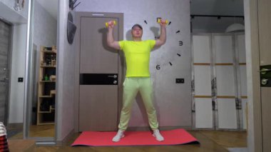 Dambıllarla omuz eklemini pompalamak. Dambıllarla evde çalış. Yavaş çekimde spor yapan bir adam..