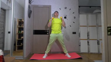 Spor salonu paspası, halterli kol salıncakları. Delikanlı evde egzersiz yaparken vücudunu esnetiyor. Dairelerde spor. Yavaş çekim