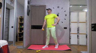 Aletlerin içinde erkek egzersizi. Fitness antrenmanı, elinde dambıllarla bir spor paspasının üzerinde. Yavaş çekim