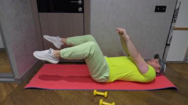 Evde, ellerinde dambıllarla, karın presi pompalarken egzersiz yapmak. Adam spor salonunda antrenman yapıyor. Yavaş çekim