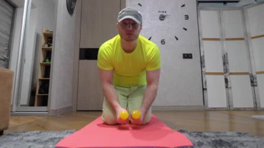 Elinde dambıllarla evde antrenman yapıyor. Omuz kası pompalayan genç bir adam. Yavaş çekim.