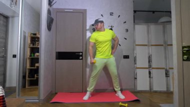 Dambıllarla omuz eklemini pompalamak. Dambıllarla evde çalış. Yavaş çekimde spor yapan bir adam.