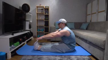 Genç sporcu ısınıyor ve vücudunu bir spor paspasına dayıyor. Evde egzersiz, egzersiz, kıvrım, yavaş çekim.