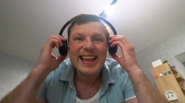 Genç mutlu bir adam evde bluetooth kablosuz kulaklıkla müzik dinliyor, kulaklıklı bir adam en sevdiği müziği dinliyor. Yavaş çekim