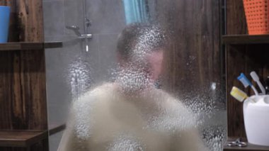 Aynaya deterjan sıkıyorum. Genç adam banyoda ayna yıkıyor, yakın plan, lastik eldiven temizleme evindeki adamın portresi. Yavaş çekim.