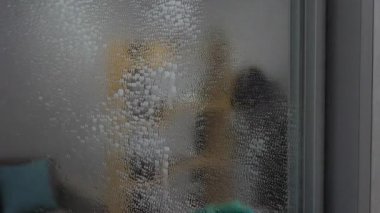 Aynaya temizleyici sprey sık. Elindeki lastik eldiven aynayı yıkar, kiri temizler. Yavaş çekim.