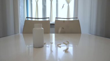 Tıbbi tabletleri beyaz bir masaya, süper yavaş çekimde, renkli tabletlerle bir bardak içme suyu ile doldurun..