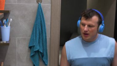  Diş fırçasıyla dişlerini fırçalayan, kulaklıkla diş macunu çalan müzik dinleyen ve dans eden yakışıklı bir genç. Yaşam tarzı. Diş sağlığı konsepti. Yavaş çekim.