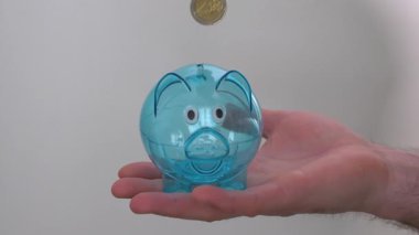 Beyaz arka planda insan eli şeffaf domuz kumbarasına para atıyor. Tasarruf kavramı, insanların mali durumu. Ağır çekim. Ekonomik kriz.