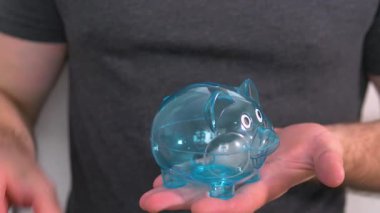 İnsan eli, şeffaf bir domuz kumbarasına bozuk para atıyor. Tasarruf kavramı, insanların mali durumu. Ağır çekim. Ekonomik kriz.