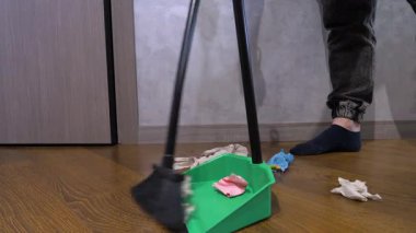 Süpürgeyle faraş süpürüyorsun, yakın plan. Bir adam evdeki bir dairede yerden toprak temizliyor, ağır çekimde.