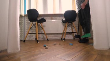 Süpürgeyle fayanslı zemindeki toprağı faraş gibi süpürüyor. Bir adam evi temizliyor, ağır çekimde.