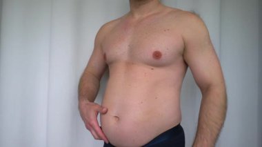 Şişman adam göbeğini gösteriyor. Gövdesi dolu çıplak bir adam sallanıyor. Yavaş çekim.