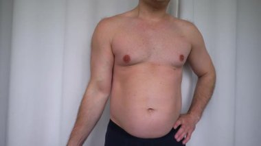  Çıplak gövdeli obez adam, küçük dambıllar komik bisepsleri pompalıyor. Beyaz arka planda, eğitimsiz bir adam dambıllarını sallıyor. Yavaş çekim