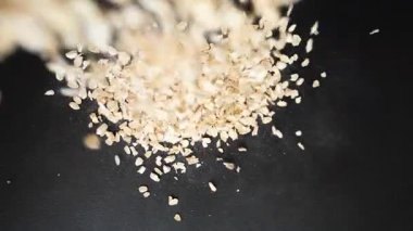 Yulaf ezmesi taneleri siyah bir masaya ağır çekimde düşer. Yiyecek taneli yulaf ezmesi.