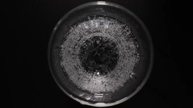 Şeffaf cam bir makroda köpüklü su içmek, siyah bir masada karbonatlı içme suyu içmek. Üst görünüm, yavaş çekim.