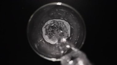 Şeffaf cam bir makroda köpüklü su içmek, siyah bir masada karbonatlı içme suyu içmek. Üst görünüm, yavaş çekim.