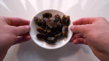  Adam kurutulmuş hurma yiyor, beyaz. Ağır çekim. Bir tabakta dilimlenmiş Kivi meyvesi.